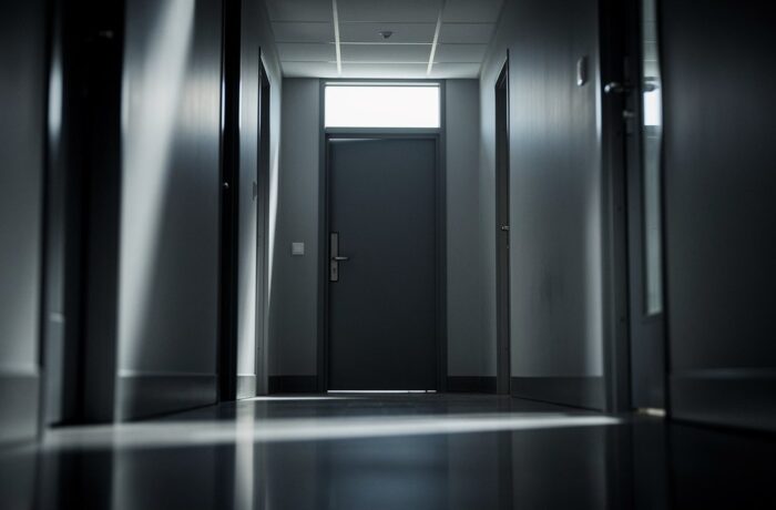 A quiet empty corridor with a closed door and soft daylight.
