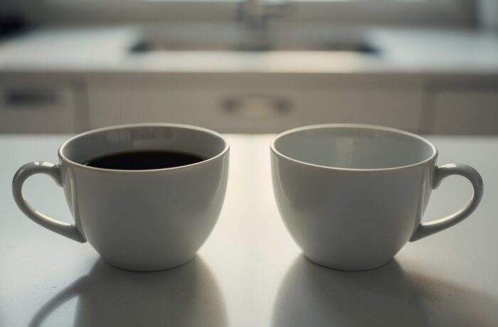 Two plain coffee cups on a softly lit kitchen bench, one full and one empty.